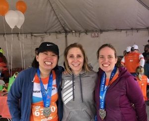 Three women stand at a finish line test, two with Mesa half marathon medals